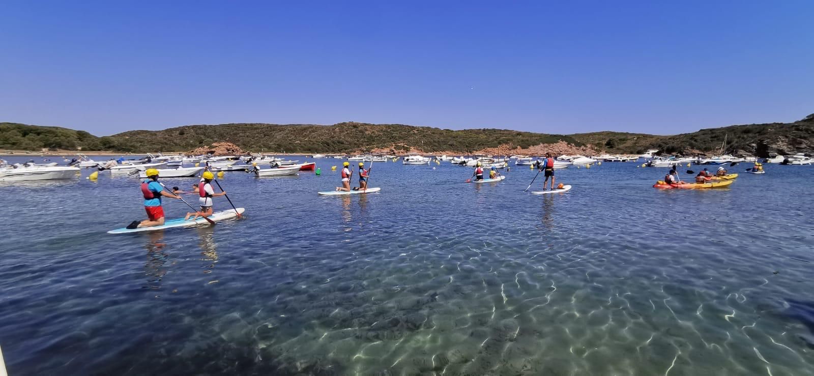 A group on paddle boards and kayaks in a clear, turquoise Menorcan bay