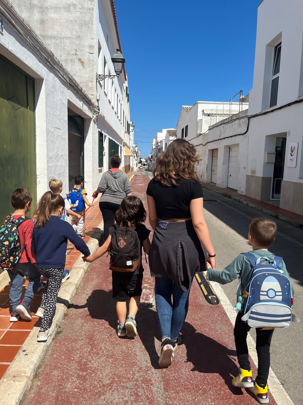 Bianka, seen from behind, walking hand in hand with young children down a white-walled street
